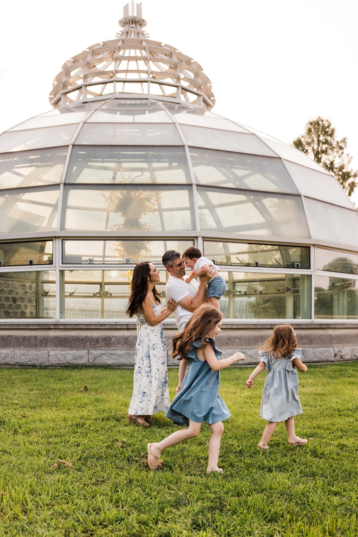 A Pittsburgh family of five enjoying a playful moment outdoors near a glass-domed structure.