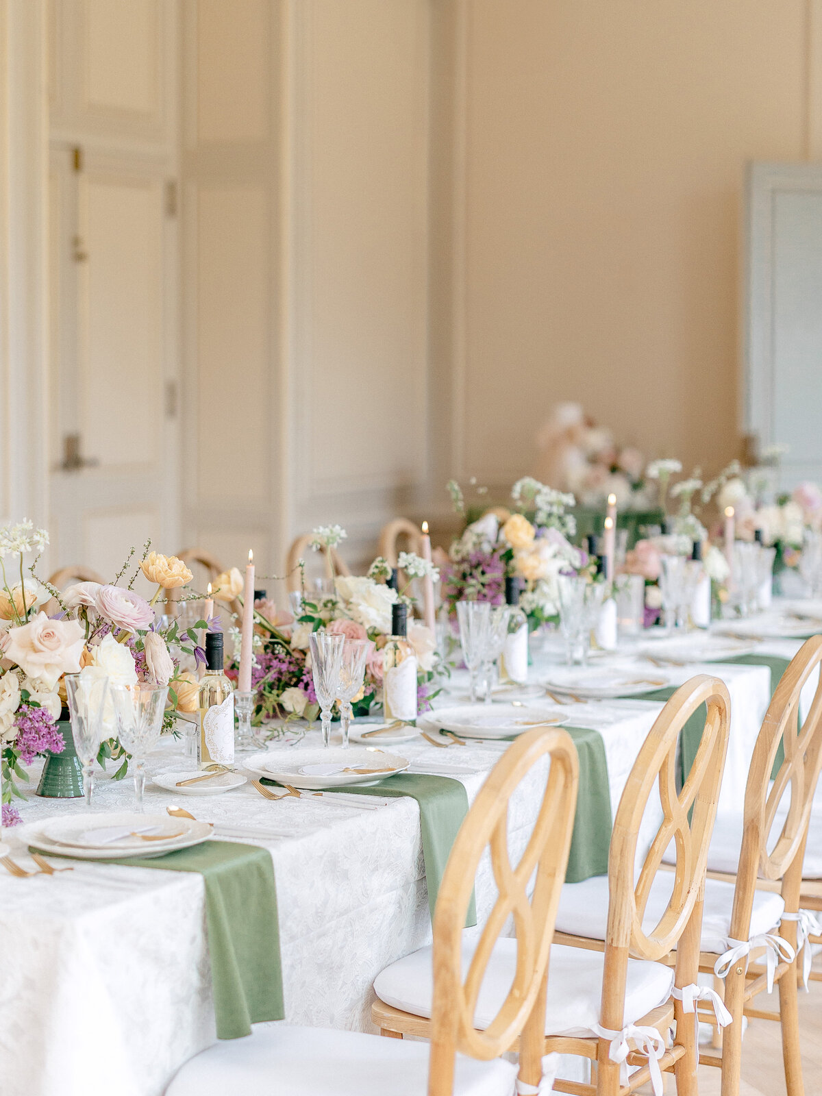 Wedding reception tables with wood chairs, green napkins, candles, and floral centerpieces