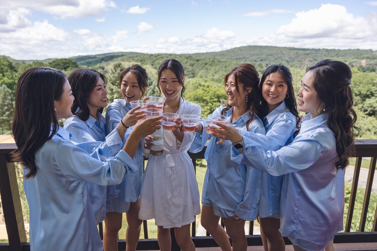 Bride and bridesmaids in blue robes popping champagne on balcony with mountain views