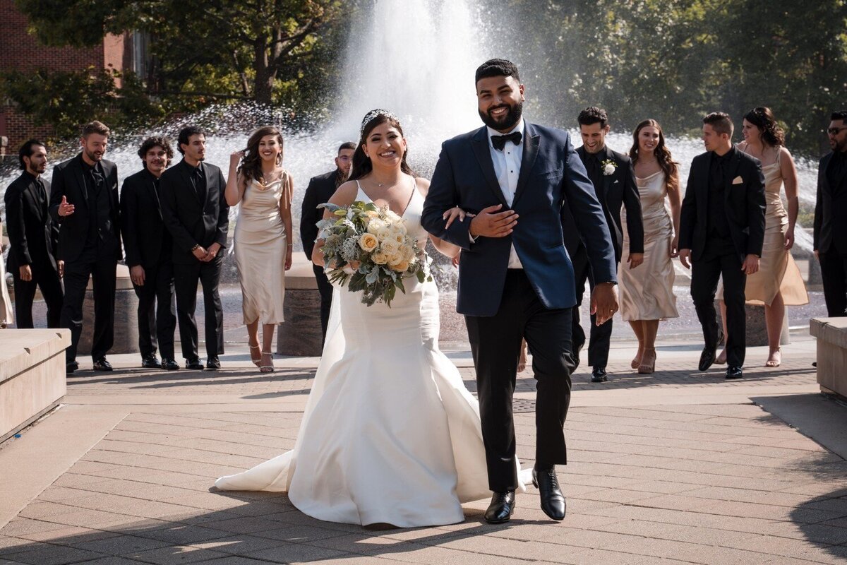 Bride and groom walk joyfully with their wedding party behind them