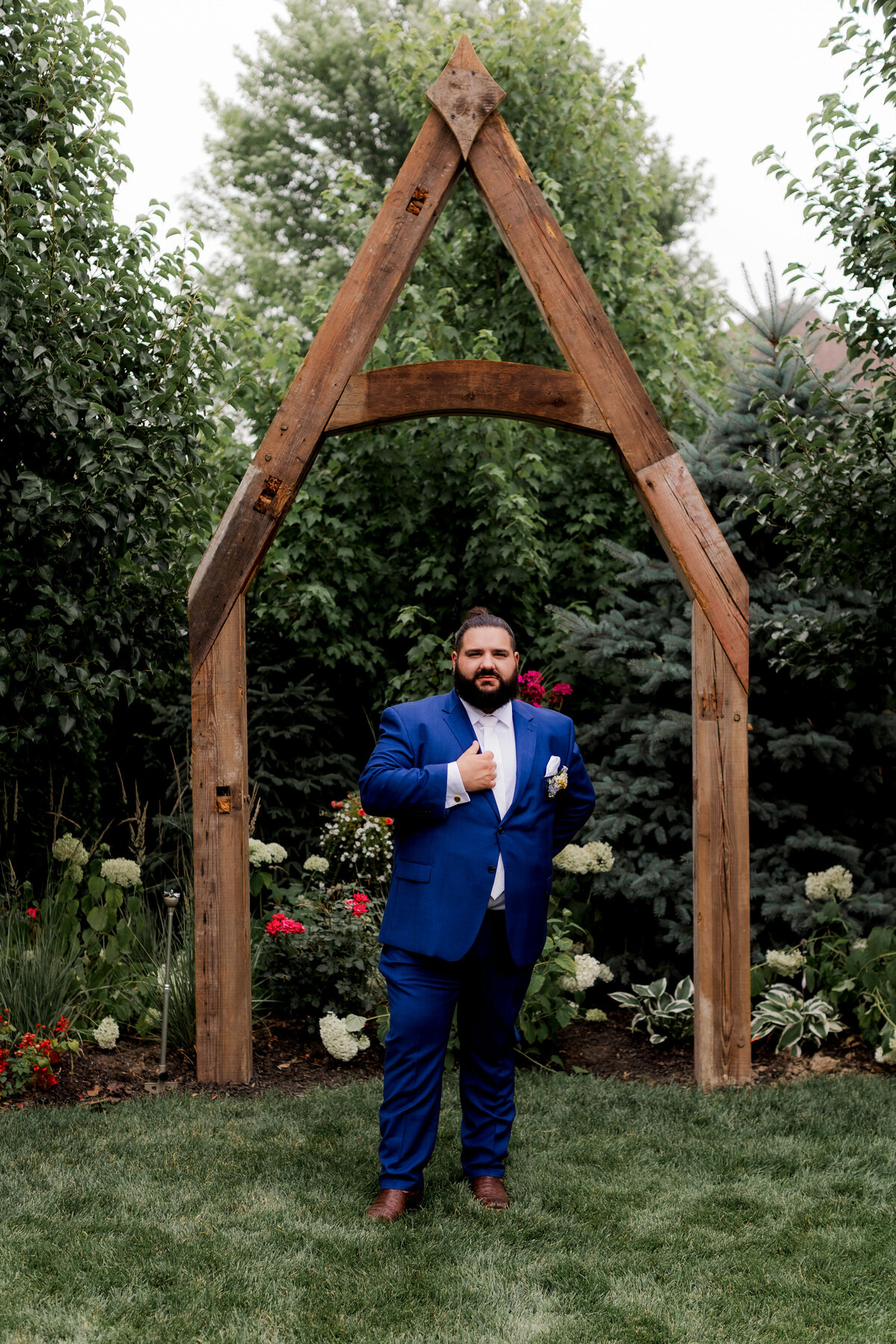 The groom holds his jacket for portrait in the garden.