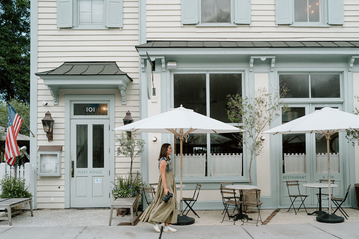Caroline, photographer, walks  in front of a building while holding her camera