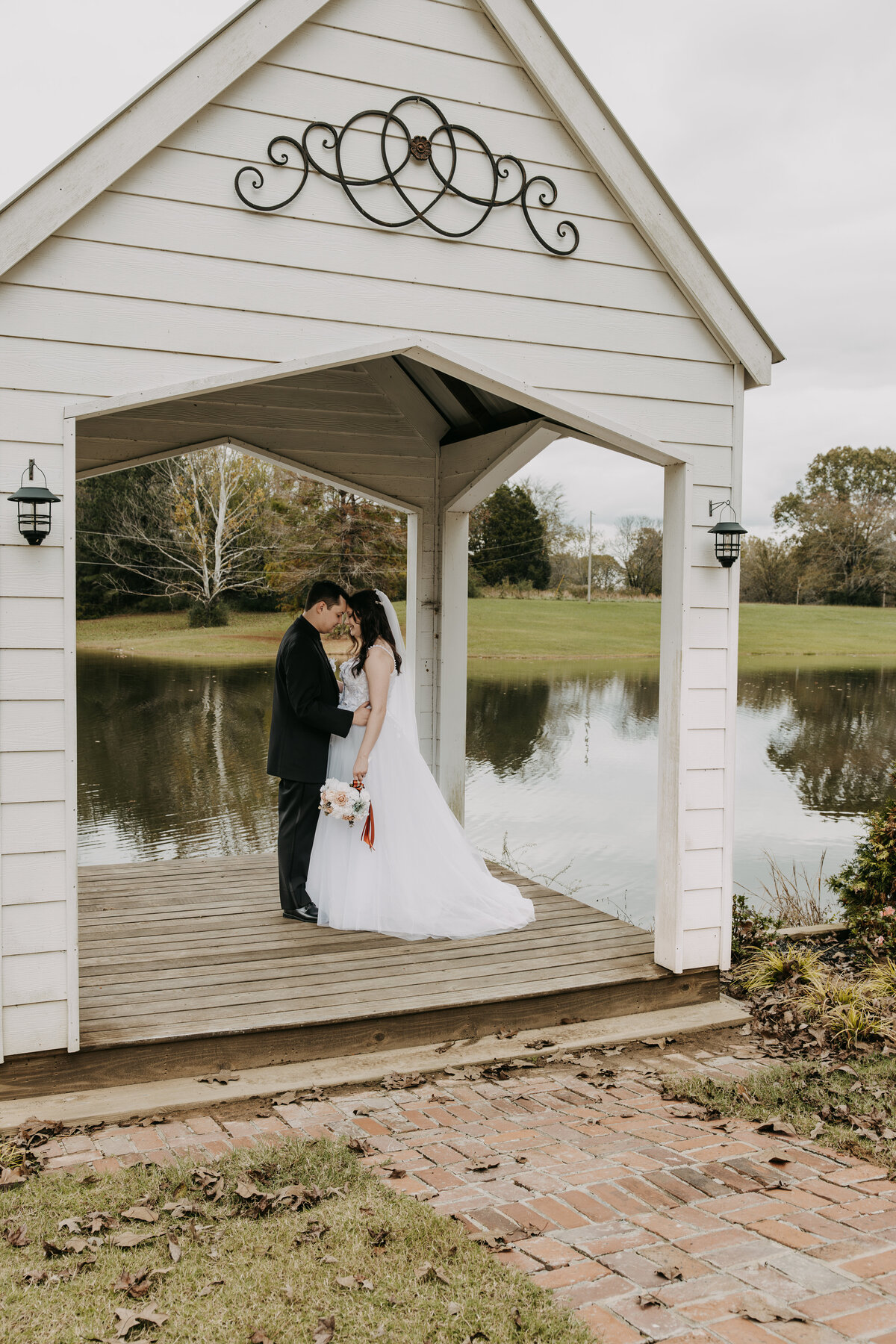 Amber and Josh, bride and groom, standing under a gazebo on a pond at Kincaid Manor in Holly Springs, Mississippi, surrounded by serene waters and lush greenery, capturing a peaceful and romantic moment.