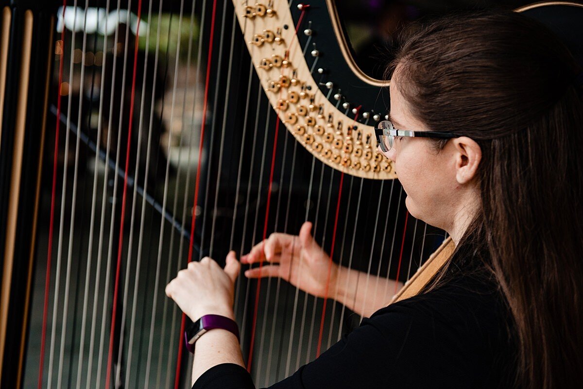 A harpist plays her gold harp with white and red strings at a wedding ceremony