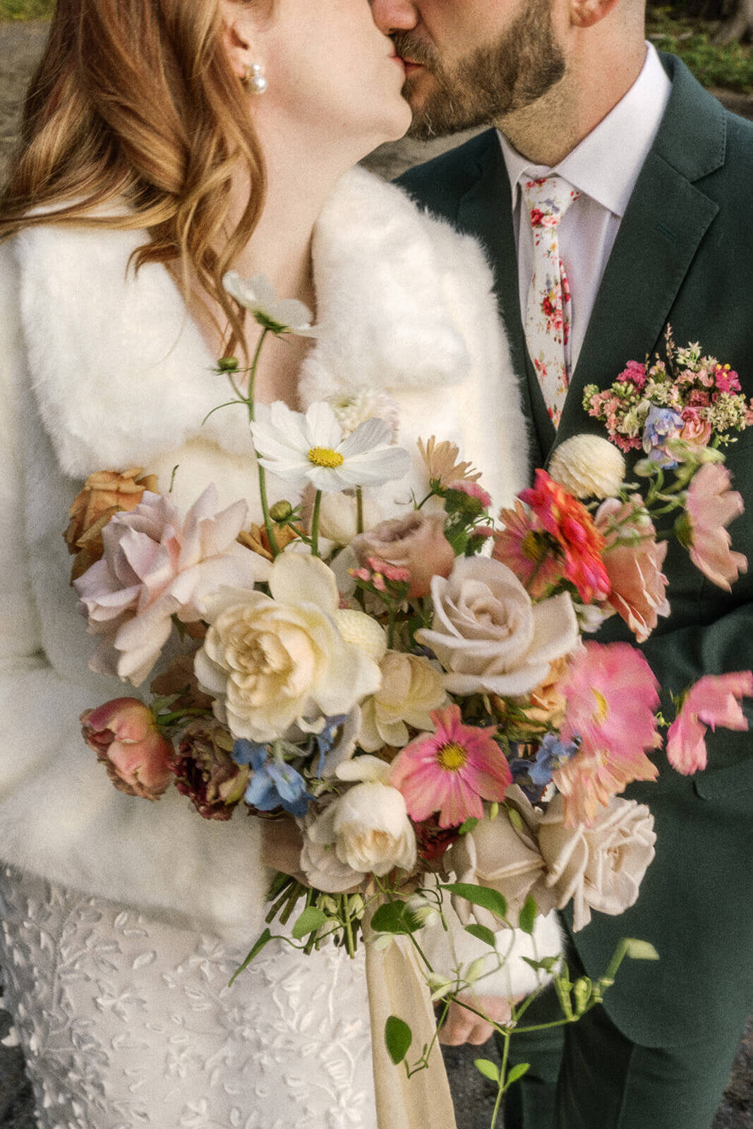 A close up of a bride and groom kissing and holding a bouquet of flowers.