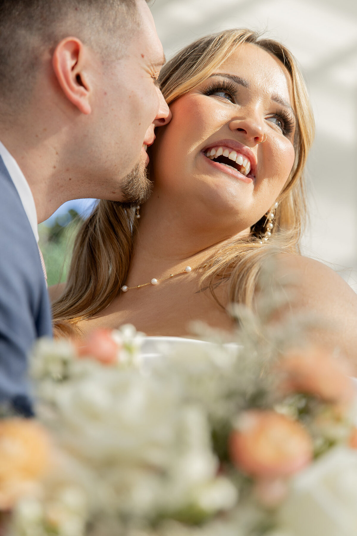 A groom kisses the cheek of his bride at their wedding. The photo is zoomed in and cropped to give a more intimate feel.