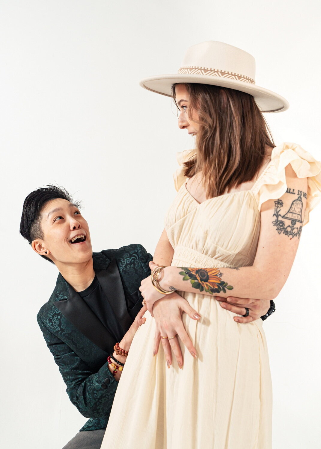 queer couple strike silly poses of faux surprise in front of a white backdrop