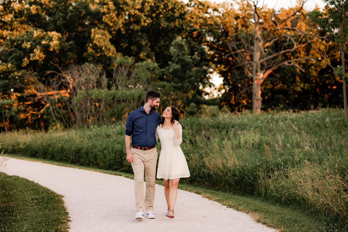 An engaged couple walks down a gravel path  holding hands.