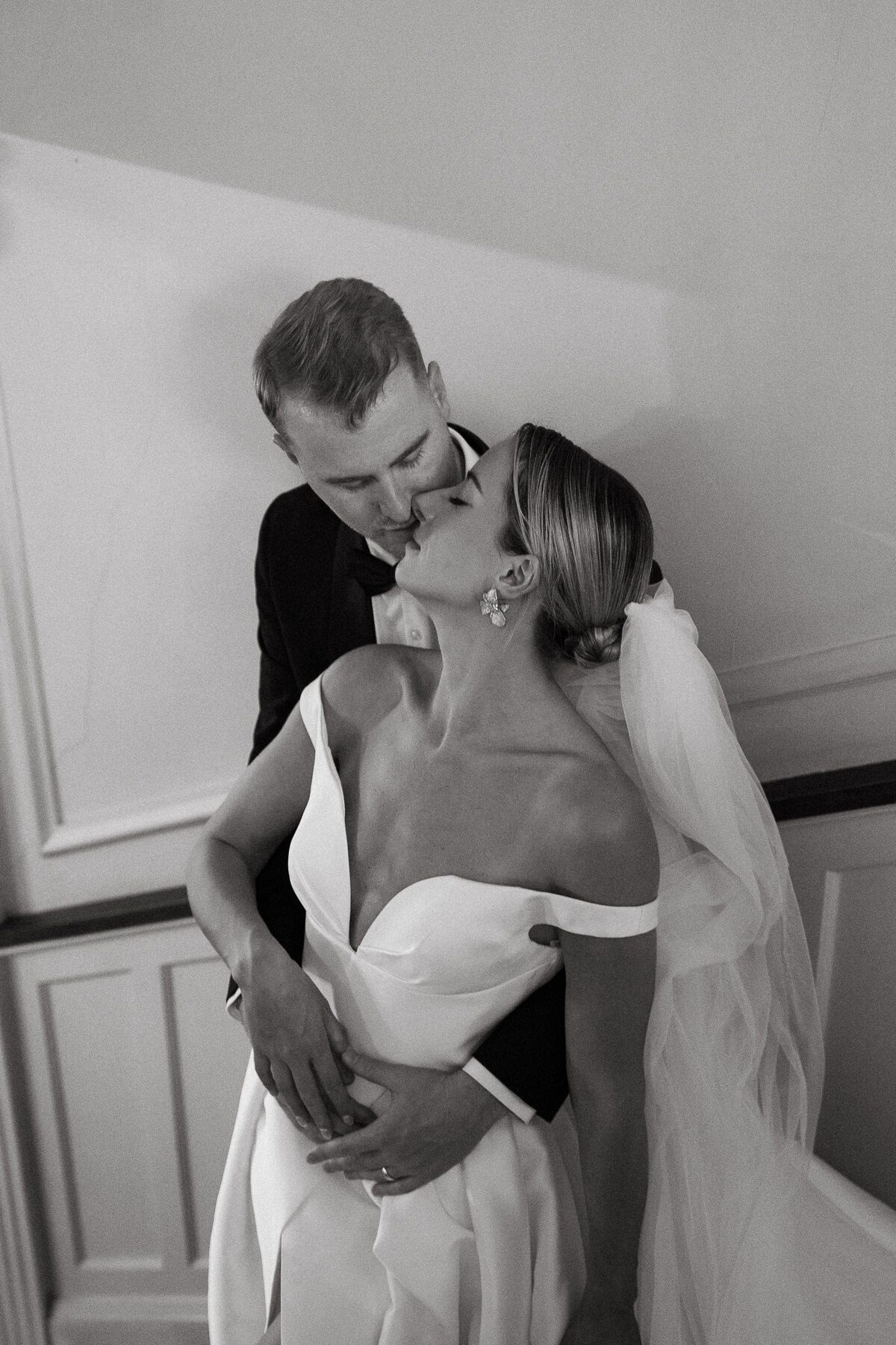 Groom standing behind bride and embracing her while she looks up at him