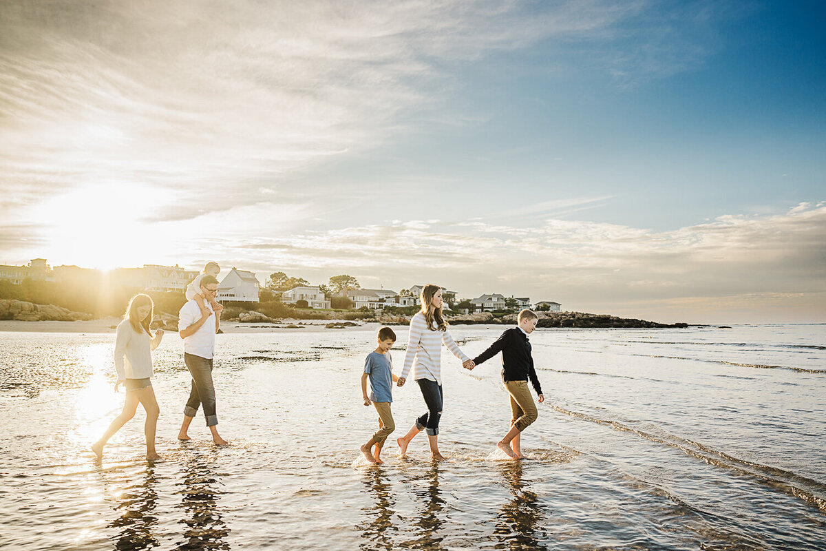 family with four kids walks in a line on a boston beach