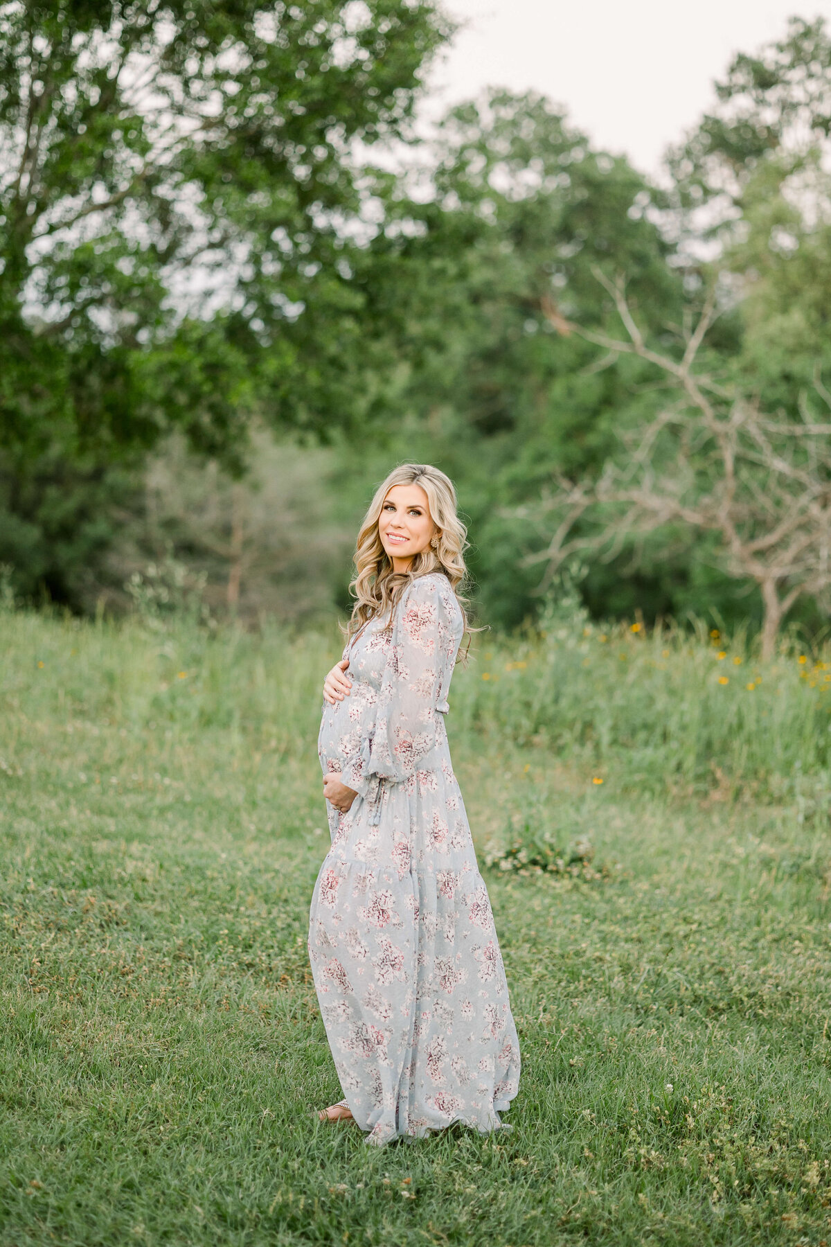 a pregnant woman standing in a field in a dress