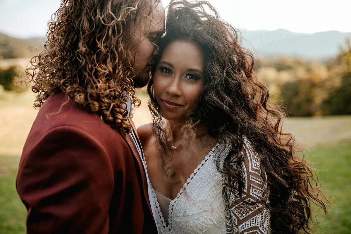 bride and groom wearing a white wedding gown and burgundy tuxedo while posing outdoors