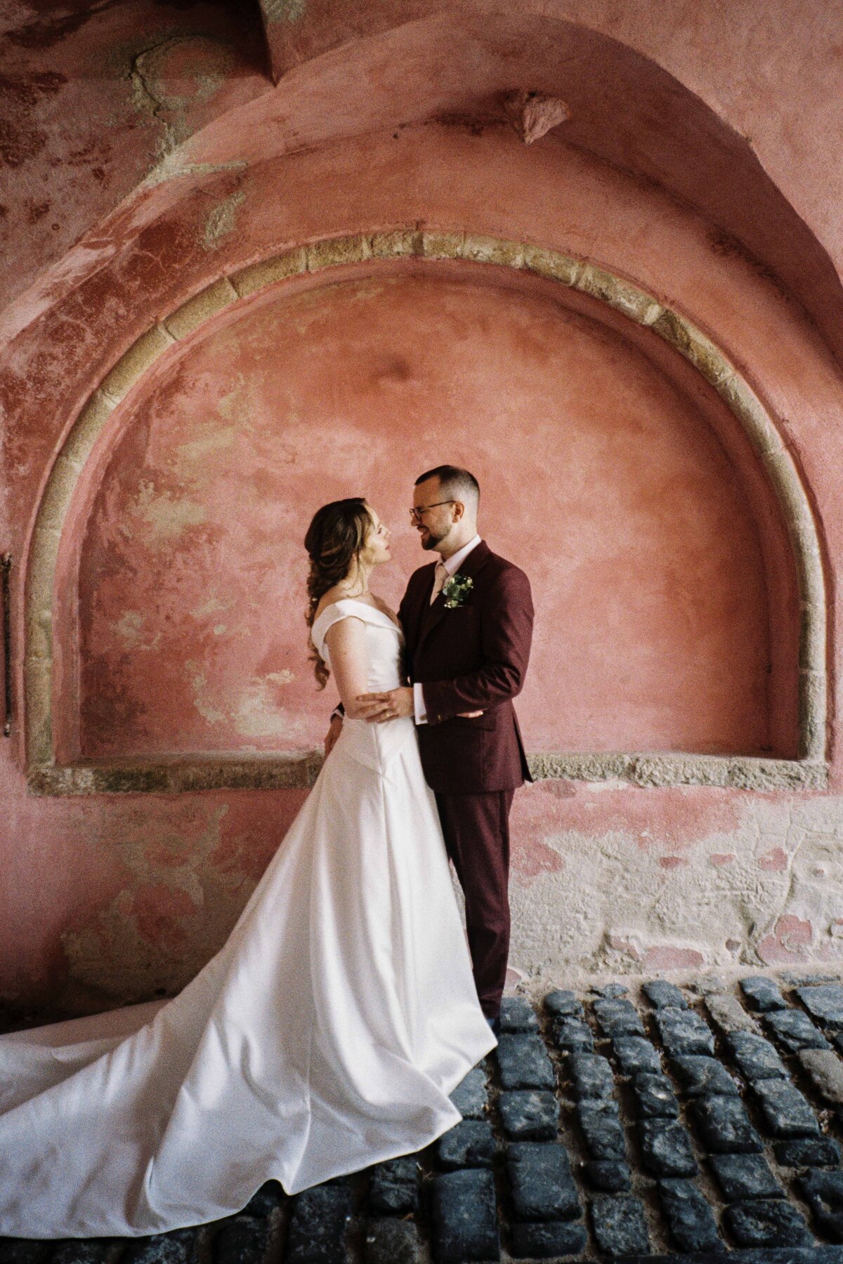 A couple stand with each other after their wedding. A large pink arch is photographed behind them. It is a 35mm film photograph.