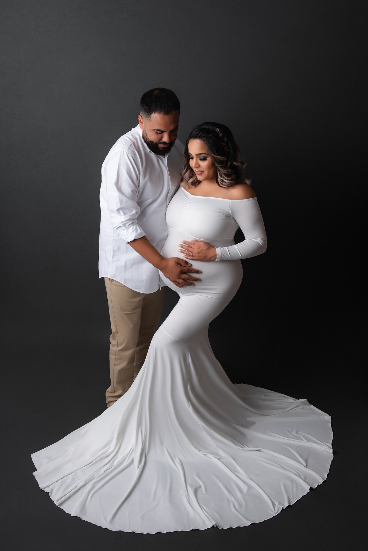 A couple maternity photoshoot studio in West Palm Beach with gray backdrop and white gown.