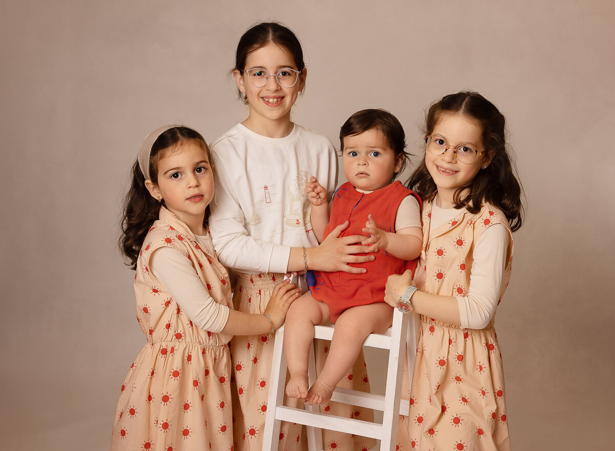 Four siblings are captured for a brooklyn ny family portrait All siblings in coordinating clothes are smiling at the camera. Captured by brooklyn family photographer Chaya Bornstein.