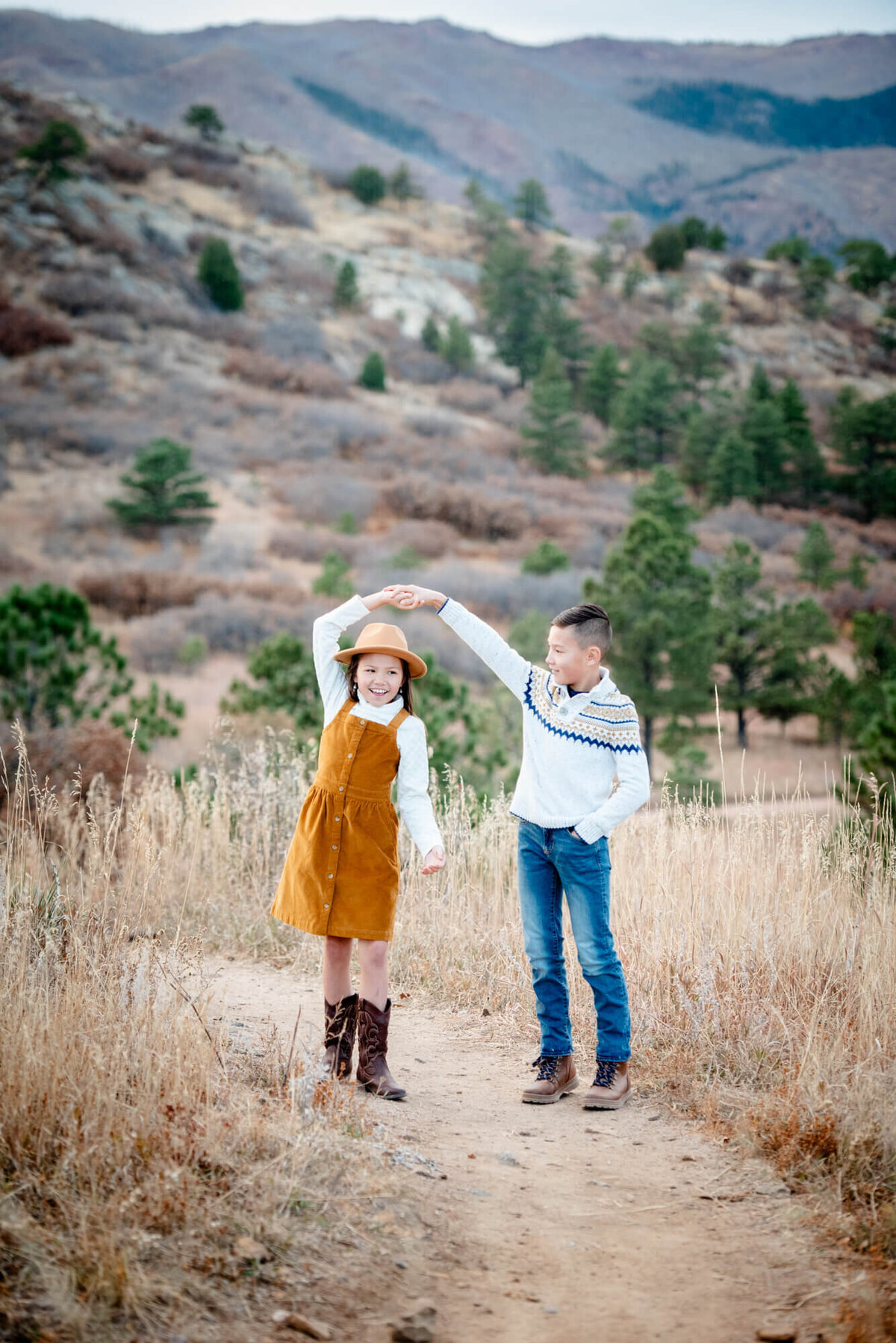A boy twirls his little sister while dancing in a trail