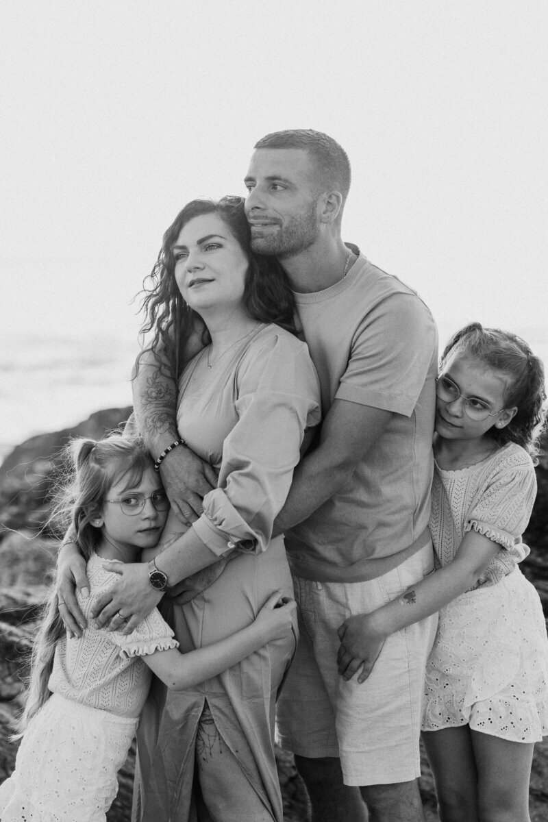 Famille immortalisée par Laura, photographe professionnelle en Vendée, se faisant un câlin général devant un décor de mer et de rochers.