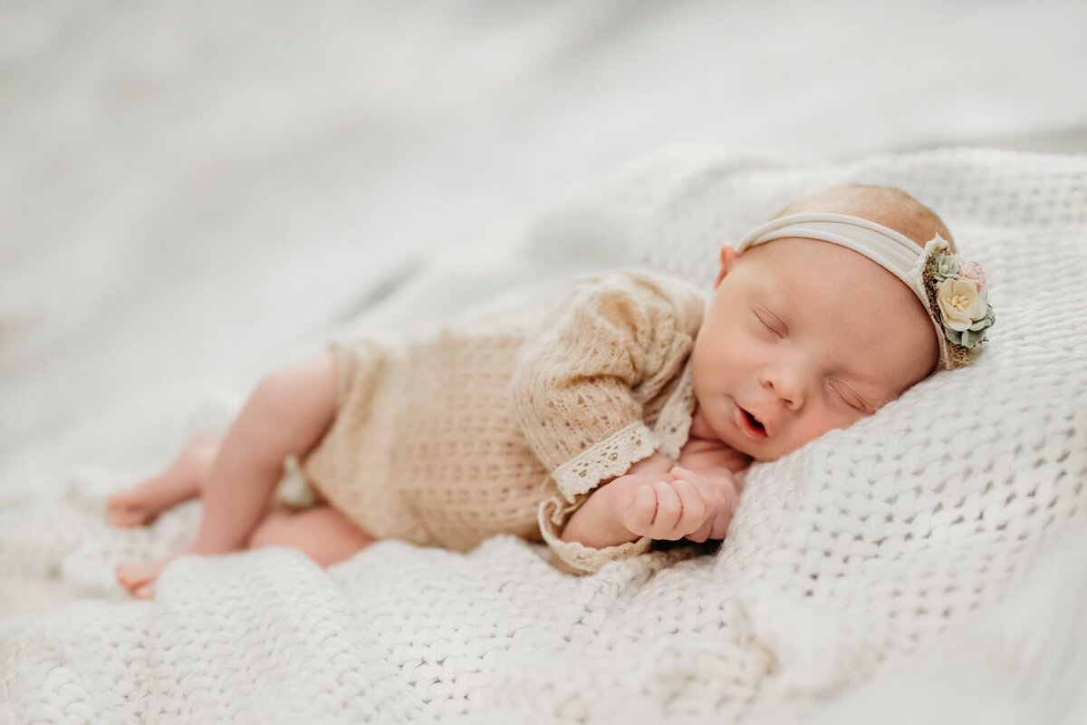 sweet newborn girl in a tan romper and cute headband for newborn photos