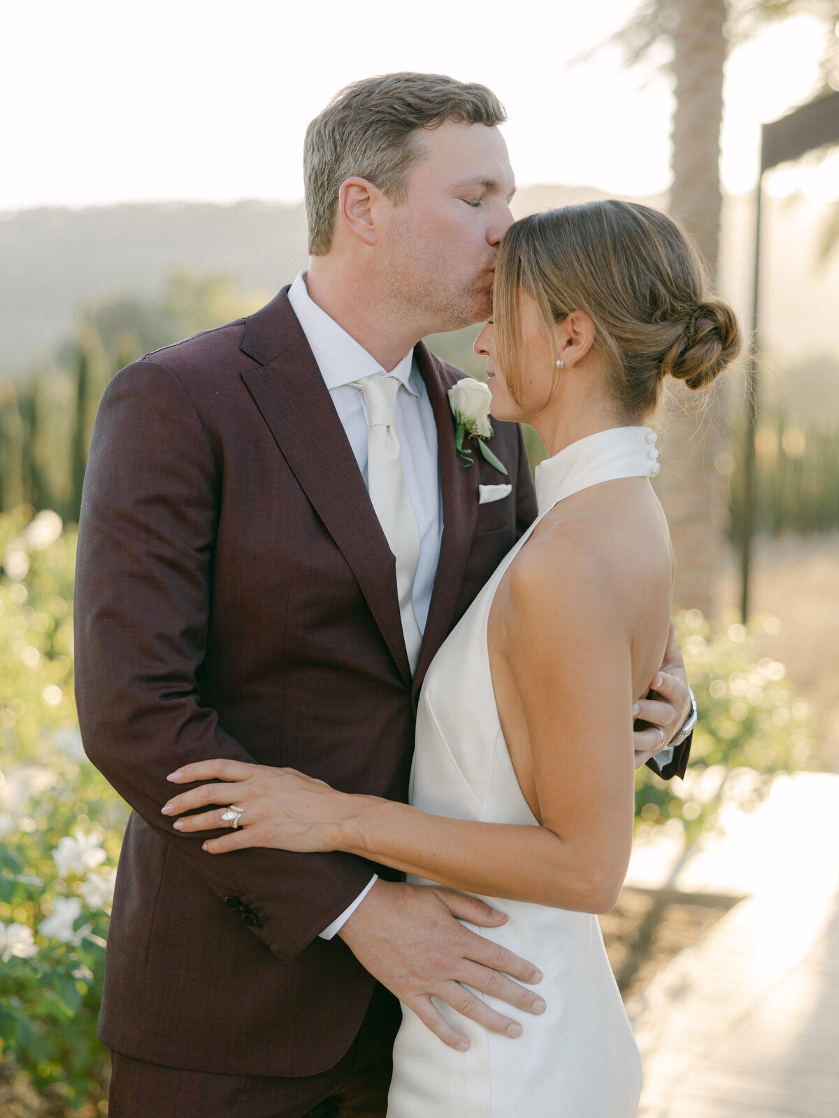 A couple sharing an intimate moment together at sunset during their wedding at Caymus Vineyards in Napa Valley. The golden light of the setting sun casts a romantic glow over the vineyards, capturing the deep connection and love shared on their special day