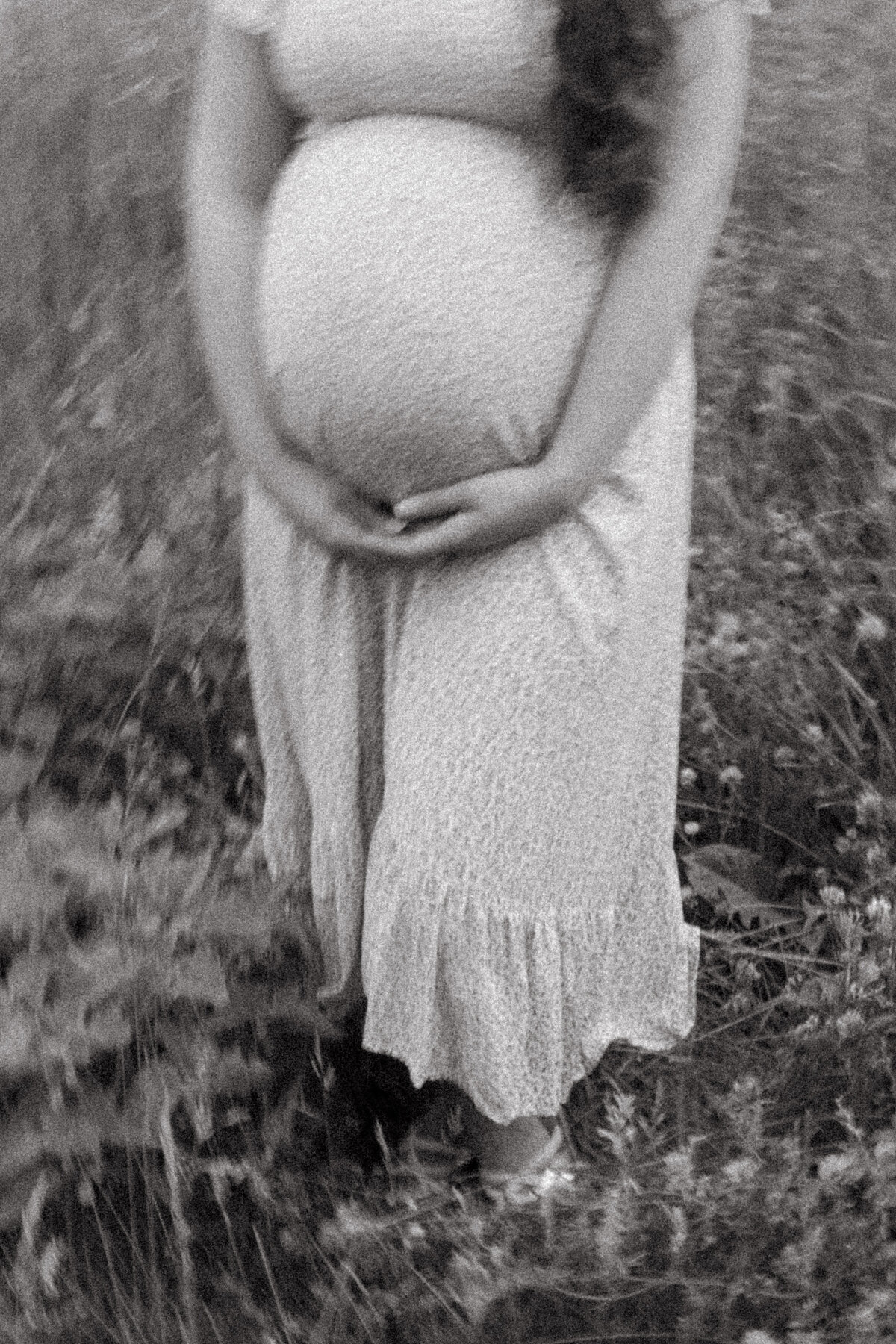 blurry black and white pregnant mother holding her belly in a grassy field