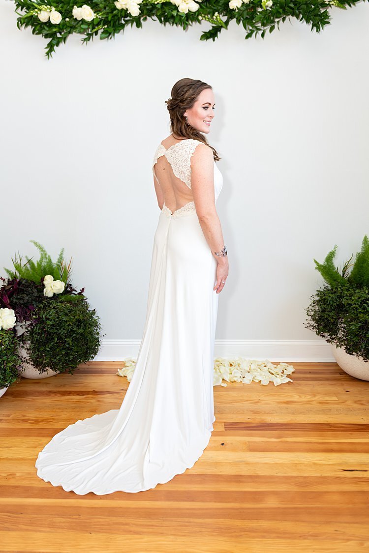 Bridal Portrait from behind showing open-backed elegant wedding gown with greenery and off-white flowers