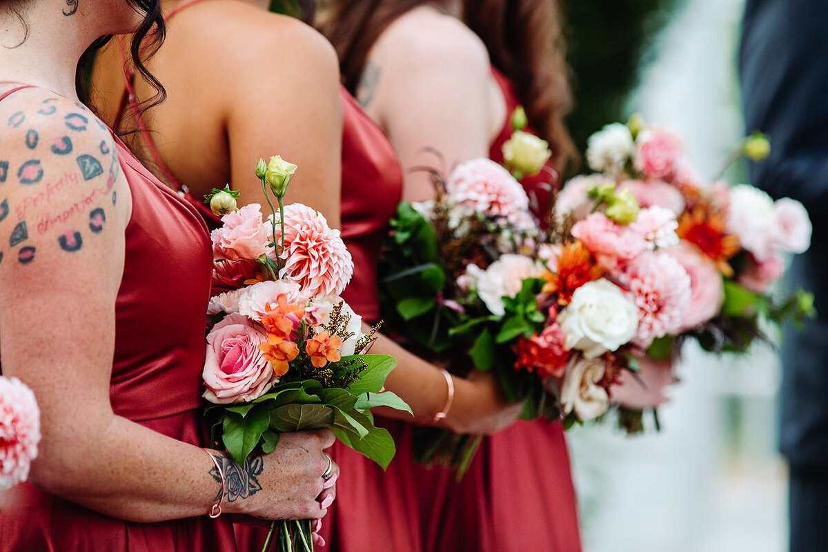 Bridesmaids hold their pink and peach bouquets in burgundy dresses.
