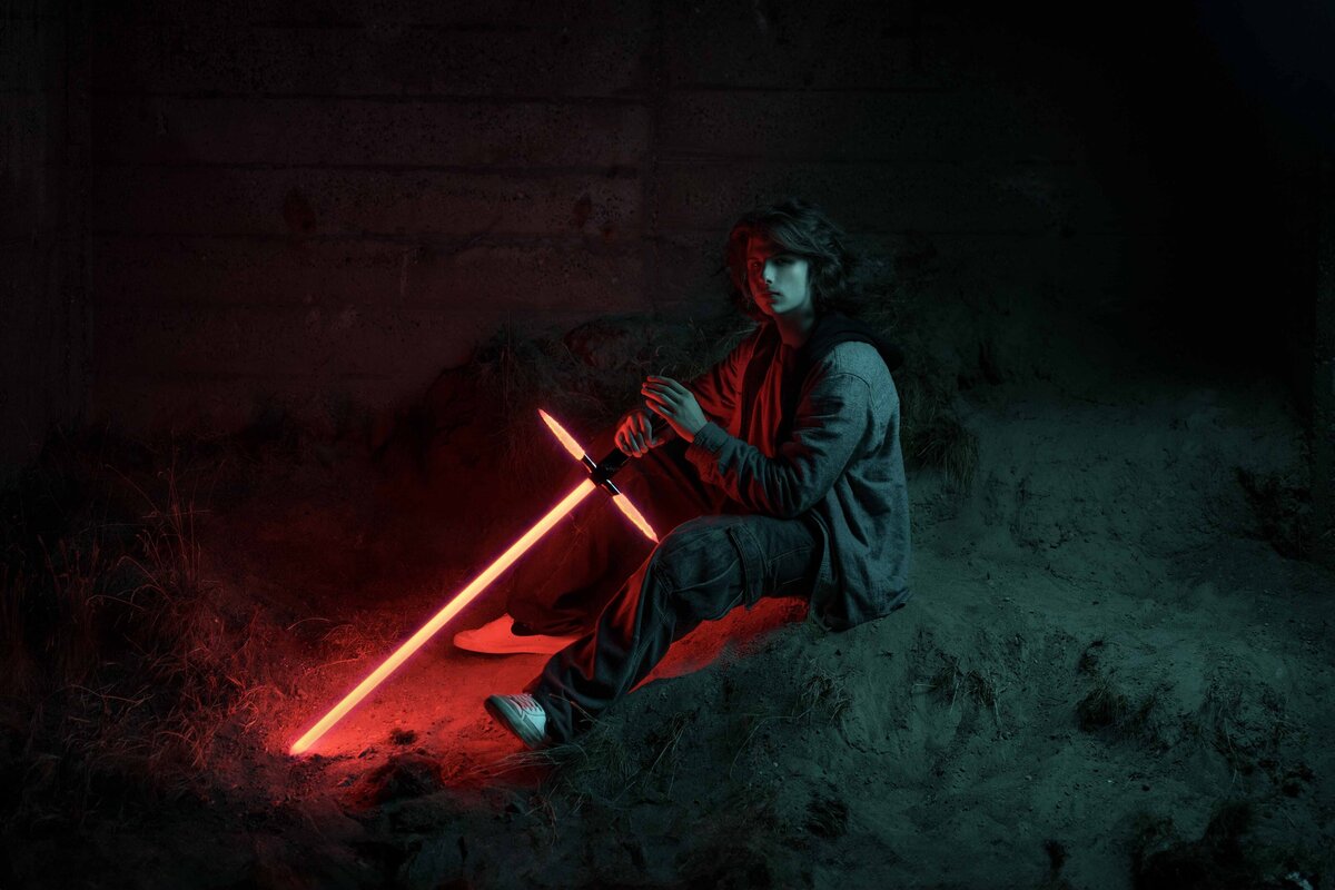 Tacoma teen boy poses with Kylo Ren style lightsaber at Chambers Bay ruins at night with gel light blue and red light from the lightsaber