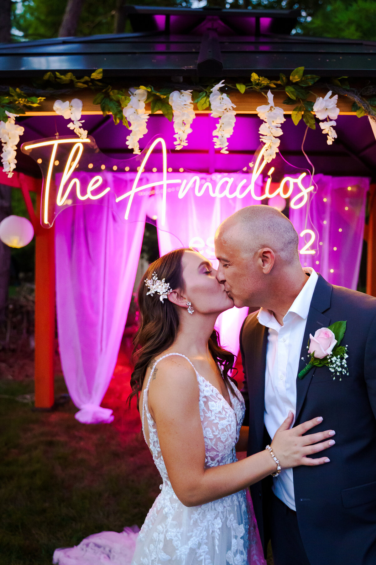 Bride and groom kiss in front of a neon sign and gazebo at night at their backyard wedding in Dublin, Ohio.