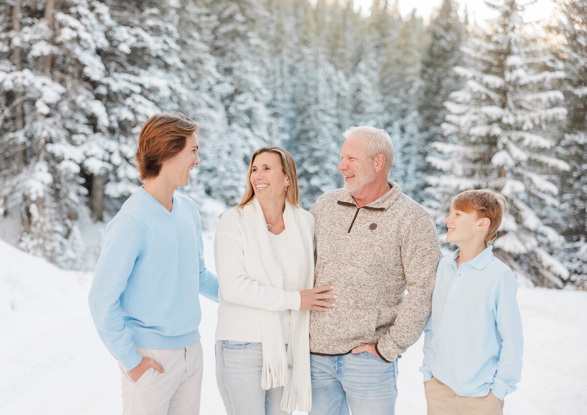 A mom and dad laugh in a snow covered mountain with their two teen sons captured by a Breckenridge Family Photographer