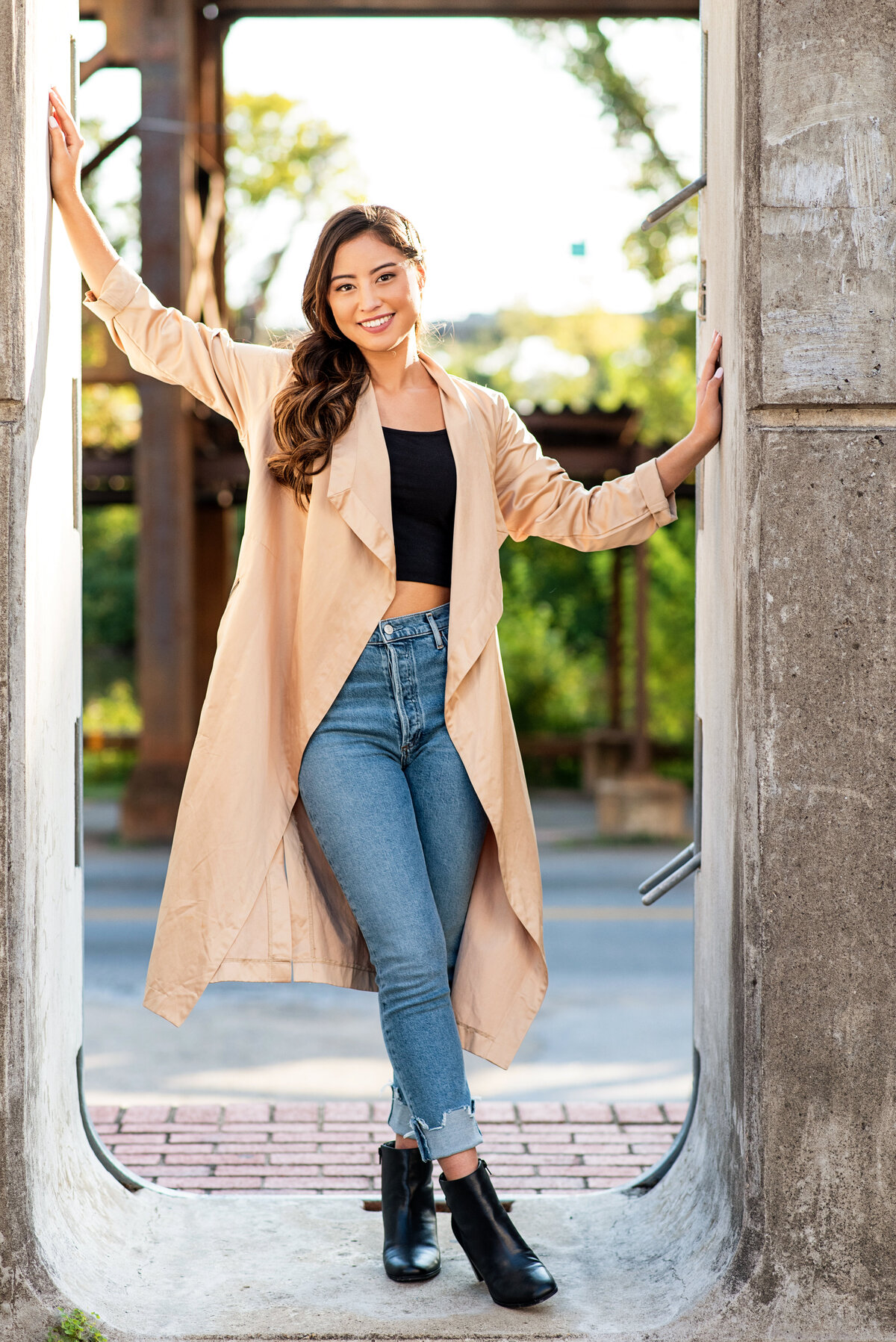 Senior girl poses in Floodwall opening Richmond, VA wearing trench coat and jeans.