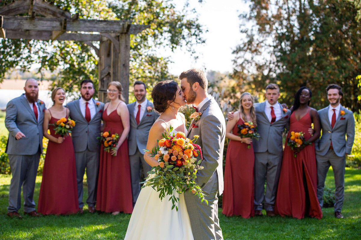 an bride and groom kiss while their bridal party looks on and cheers in the background.  Captured by Ottawa wedding photographer JEMMAN Photography