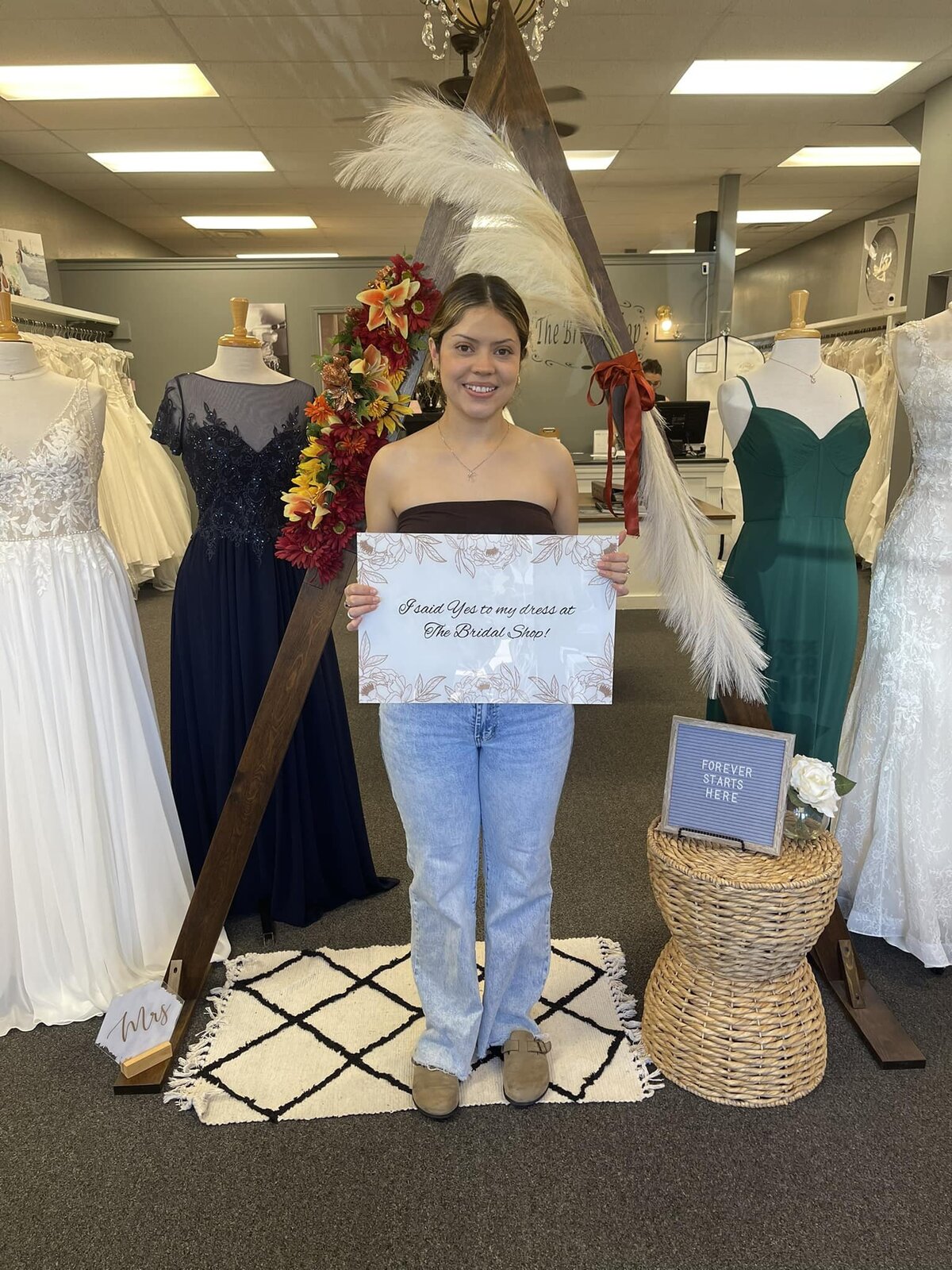 Woman standing in a bridal shop holding a sign after saying yes to her dress