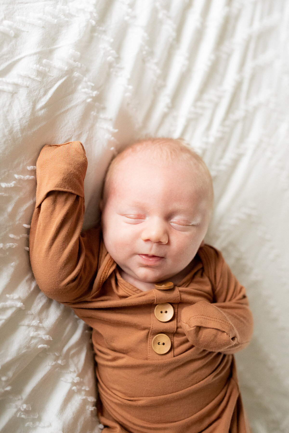Newborn baby boy wearing light brown sleeper laying on white comforter sleeping.  Photo by Portland newborn photographer.