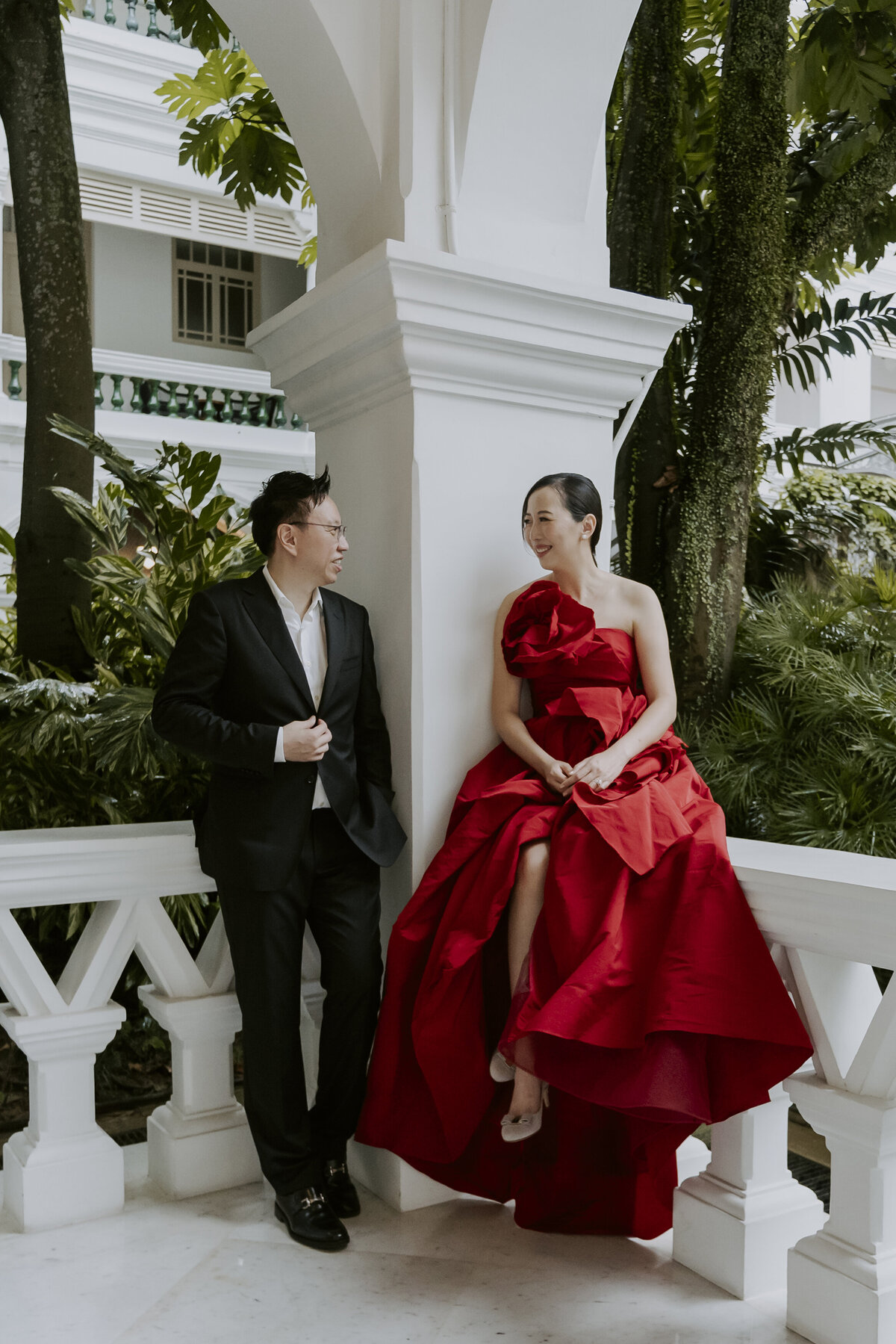 a woman in a red dress and a man in a black suit sit on the porch  and look at each other