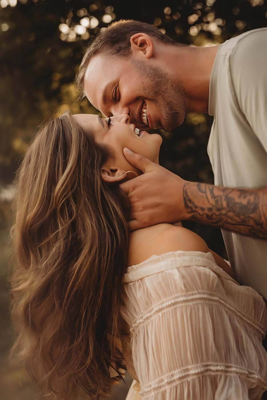 A husband holds his wife head while they are smiling at each other with their eyes closed