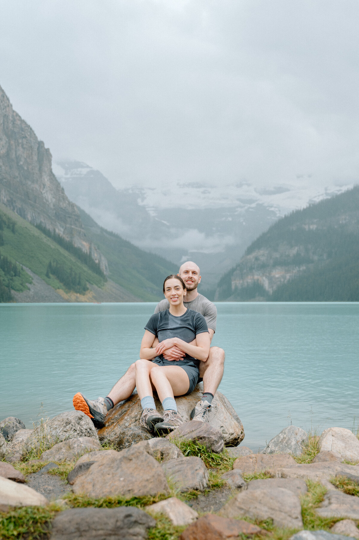 romantic photo of couple sitting on some rocks with lake louise in the background.