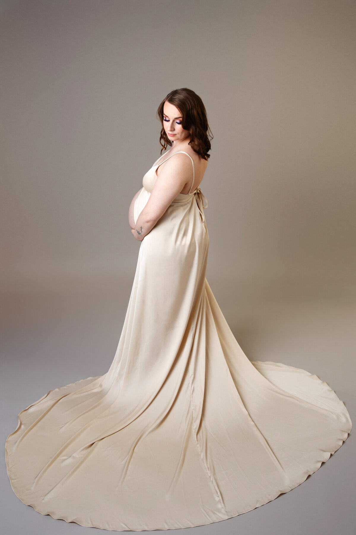 Pregnant woman wearing a long gold gown looking back over her shoulder