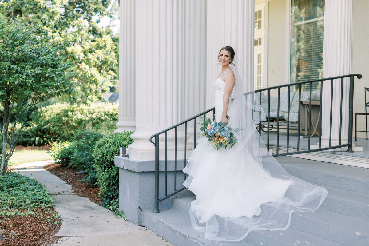 A bride smiles at the camera while standing by a white column.