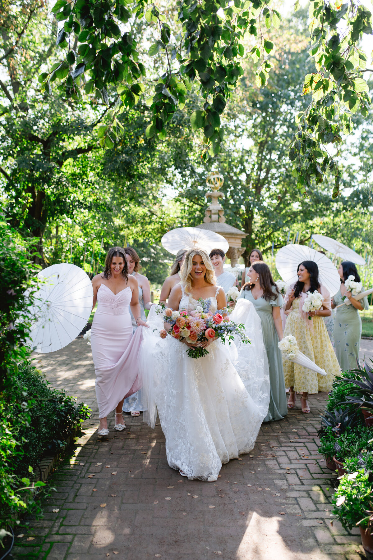 Bride walking with bridesmaids under large white balloons in a lush garden.
