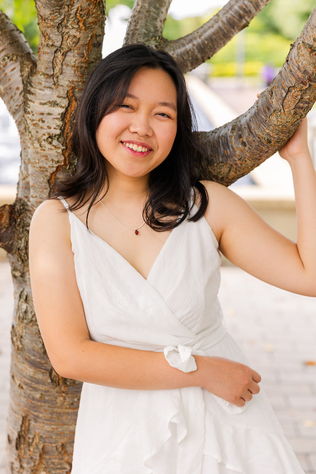 teenage girl leaning agains a tree wearing a white dress one hand holding a branch during portrait photo session