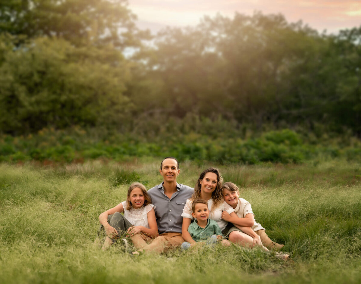 A mom, dad and their children sitting in the tall green grass and smiling for a portrait with an Asheville Family Photographer