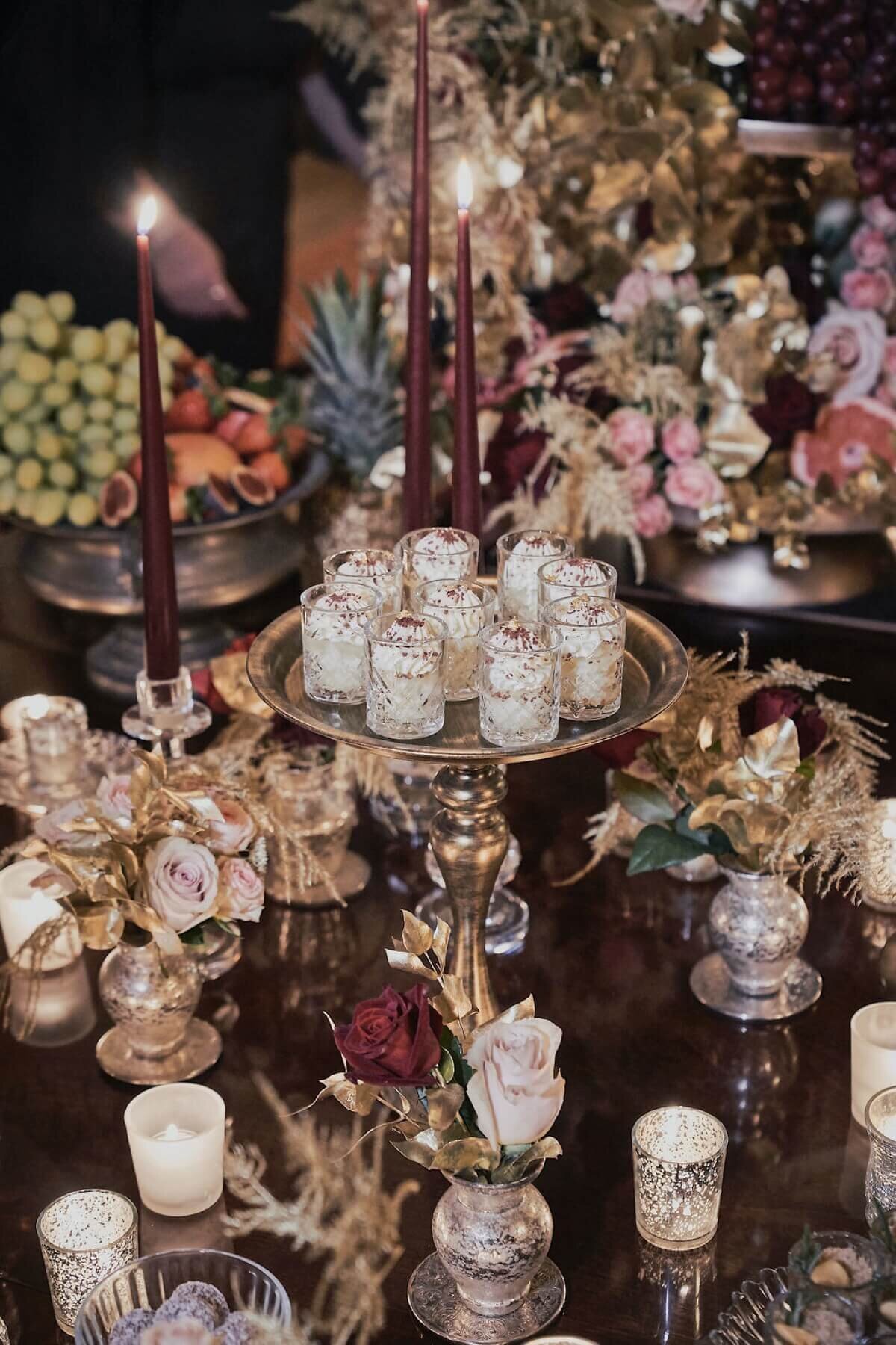 mousse shooters on a gold cake stand with candles and small flower votives, maroon taper candles