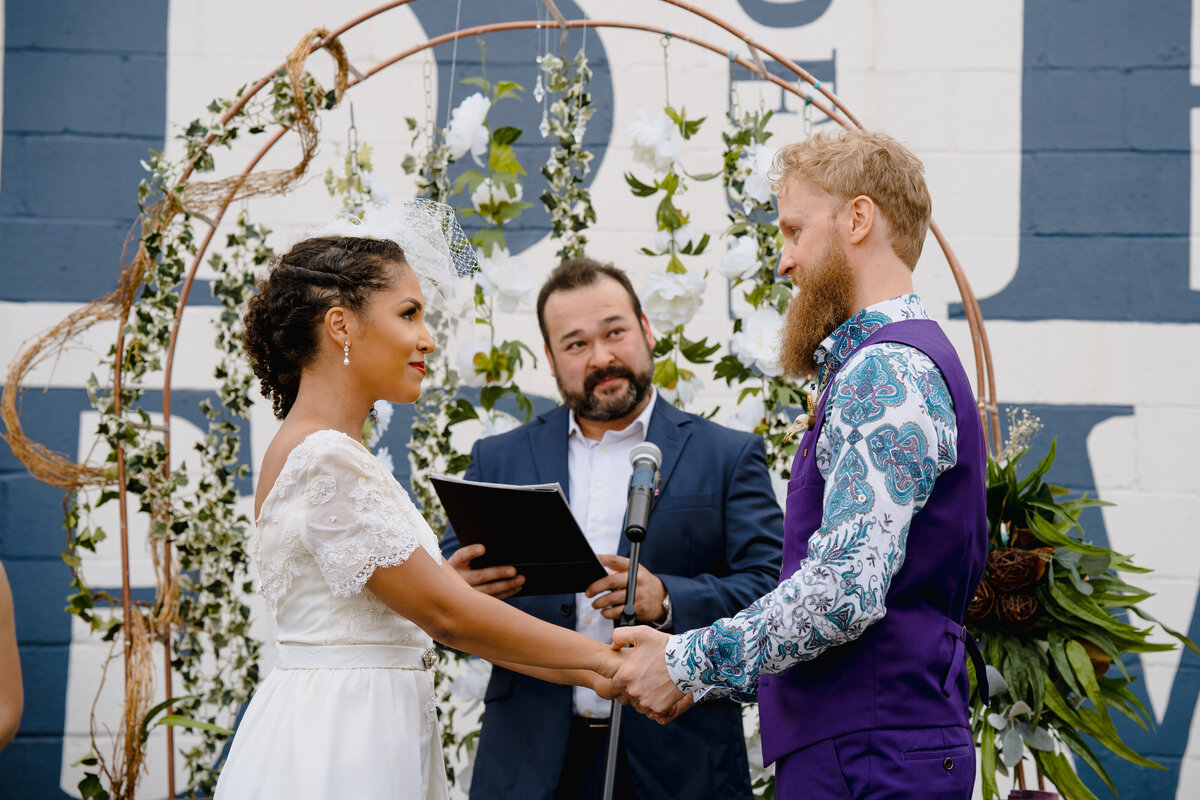 A couple holding hands while standing up at their wedding with their officiant behind them.