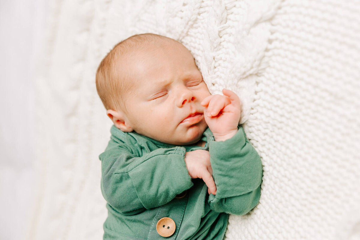 Sleeping 8 day old baby boy wearing a green outfit.