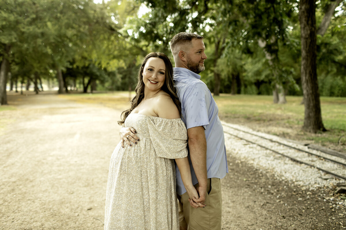 A romantic maternity photo of mom and dad standing together at Trinity Park, holding hands and sharing a loving gaze, captured by Chunky Monkey Photography.