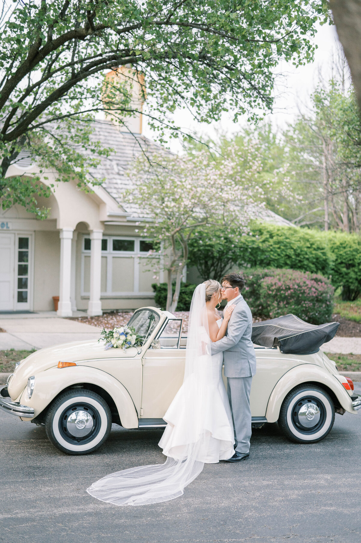 Bride and groom pose in front of vintage car at midwest wedding