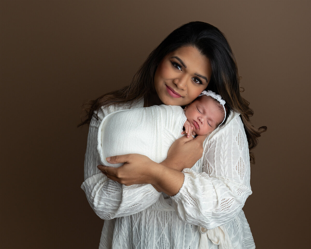 An intimate mother and baby portrait taken in the studio, showing a mother holding her newborn daughter wrapped in soft white swaddling. Photographed at Meraki Photographic Creations in Paris, Ontario.