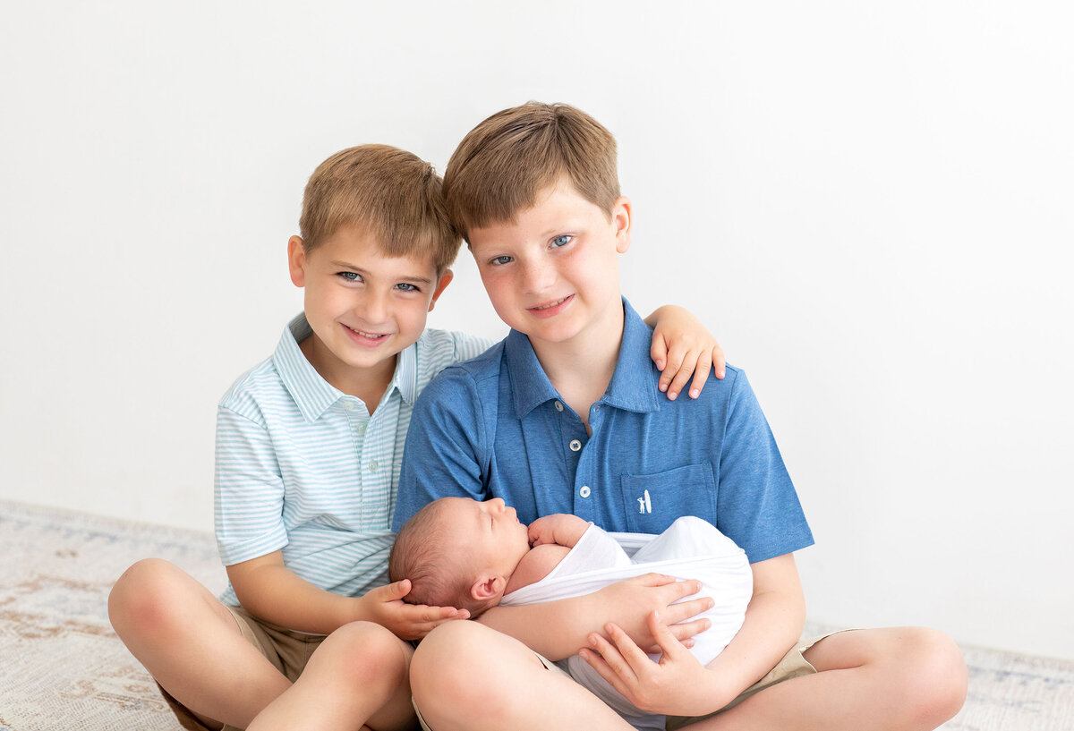 older brothers hold their new baby sibling gently during their Bucks County newborn session with Ivory Tree Portraits.