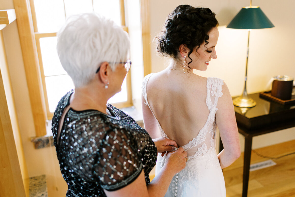 mom helping bride put on her dress