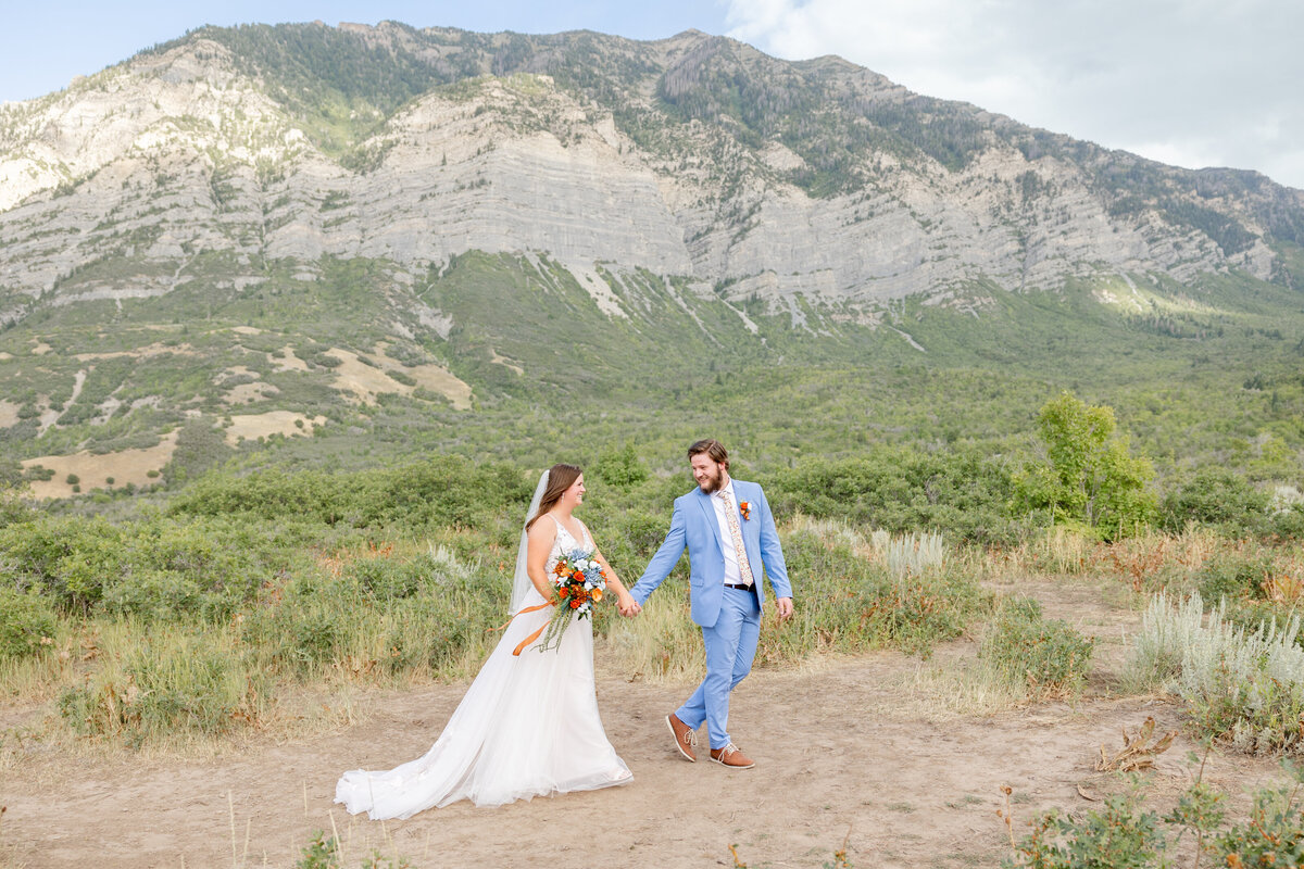 The groom joyfully leads his bride up a path, showing the beautiful mountain view in the background.
